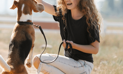 Young woman using positive reinforcement techniques during a puppy obedience training session outdoors with a Beagle puppy.